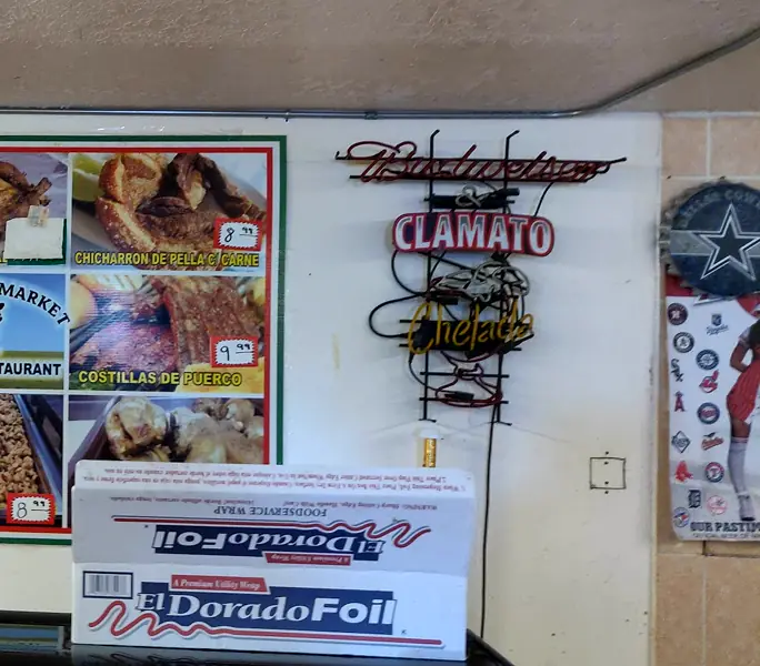 The wall poster menu with carnitas, chicharrón and ribs, next to a Clamato neon sign.