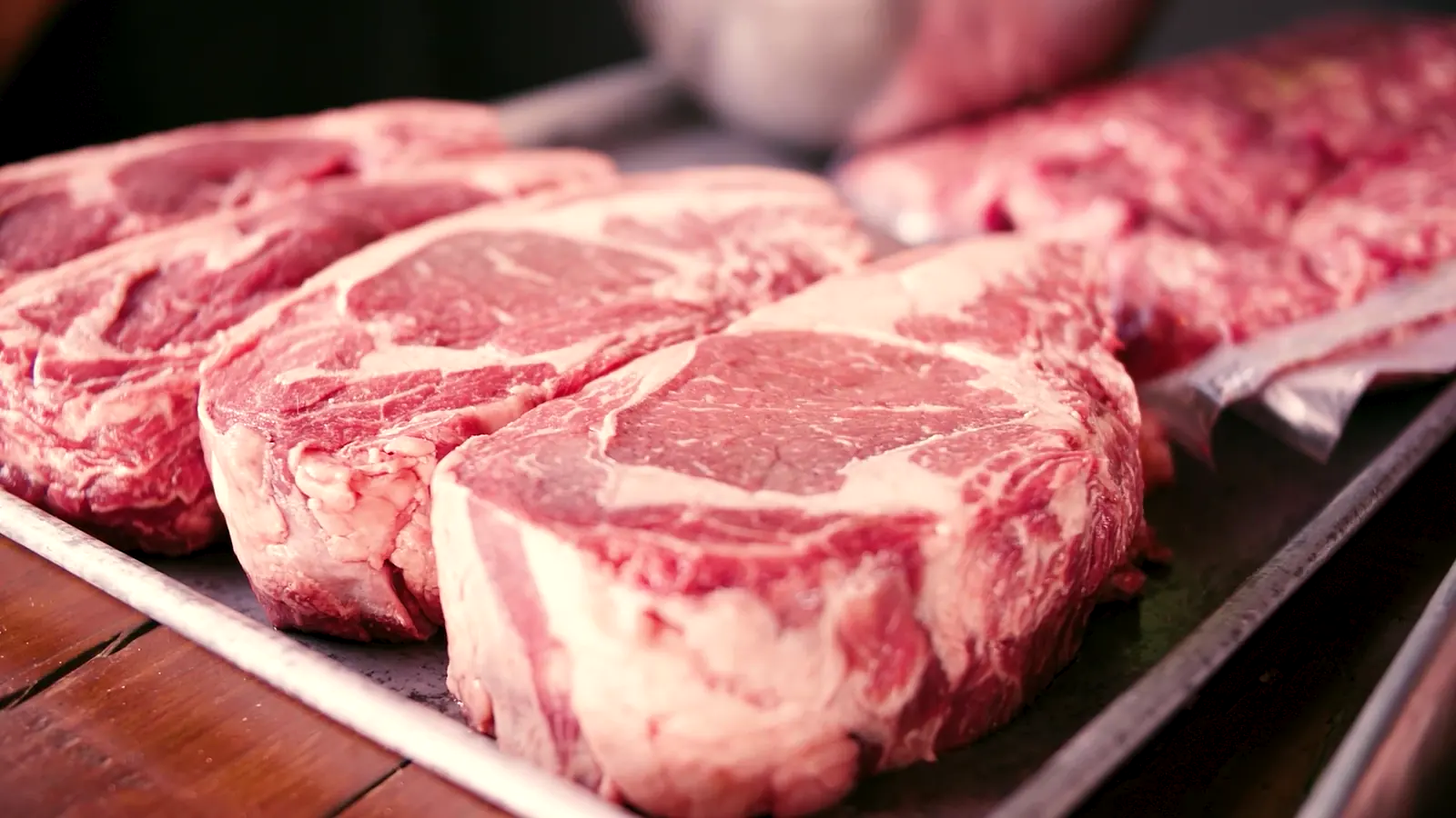 Raw marbled ribeye steaks lined up on a tray.