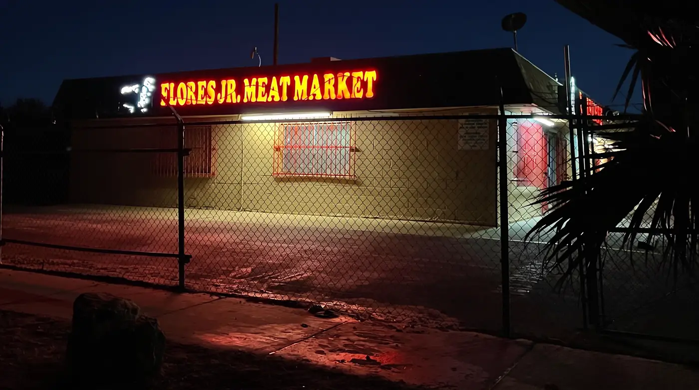 The Flores Jr. Meat Market neon sign glowing red and yellow at night.