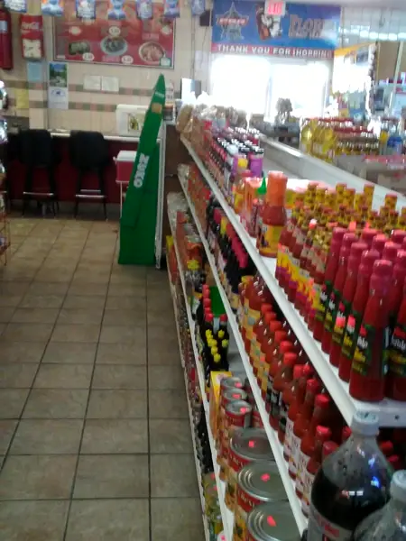 An aisle of hot sauces and sodas, with red chairs at the back.